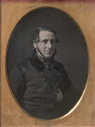Homem de meia-idade com barba em tiras, jaqueta abotoada enfiada à mão, anos 1840-50