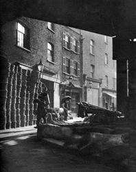 Cestas de frutas empilhadas contra casas no Borough Market, Londres, 1926-1927.
