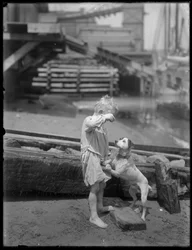 Menino descalço, possivelmente William Gray Hassler, brinca com cachorro na margem de um rio ou lago, Nova York, c.1910