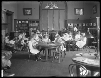 Crianças lendo na sala de leitura de um ramo não identificado da Biblioteca Pública de Queens Borough, c.1910