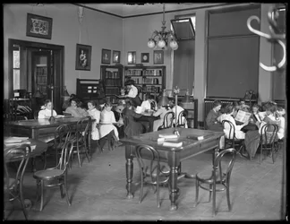 Crianças lendo na sala de leitura de um ramo não identificado da Biblioteca Pública de Queens Borough, c.1910