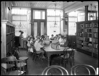 Crianças lendo na sala de leitura de um ramo não identificado da Biblioteca Pública de Queens Borough, c.1910
