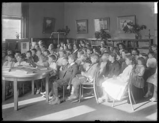 Crianças sentadas, ouvindo na sala de leitura de um ramo não identificado da Biblioteca Pública de Queens Borough, c.1910
