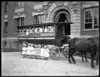 As meninas pequenas colocam dentro e na frente de um vagão puxado por cavalos, na frente de um edifício não identificado, provavelmente o asilo órfão católico romano, Kingsbridge, Bronx, c.1910